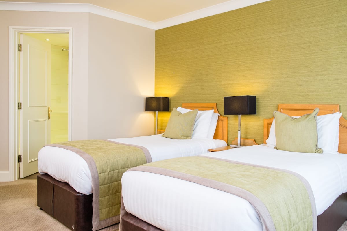 Une chambre d’hôtel avec deux lits, une tête de lit en bois, des lampes de chevet et une porte donnant sur une salle de bain.