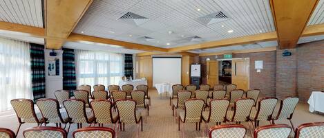 A conference room with rows of patterned chairs, a white table with a projector, and a brick wall.