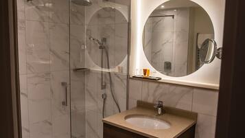 A modern bathroom with a glass-enclosed shower, a wooden vanity, and a round mirror.
