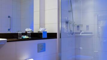 A modern bathroom with a glass-enclosed shower, a toilet, and a sink with a mirror above.
