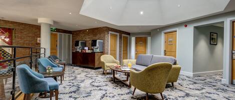 Un vestíbulo de hotel con techo alto, una recepción, zonas de estar y una alfombra estampada.