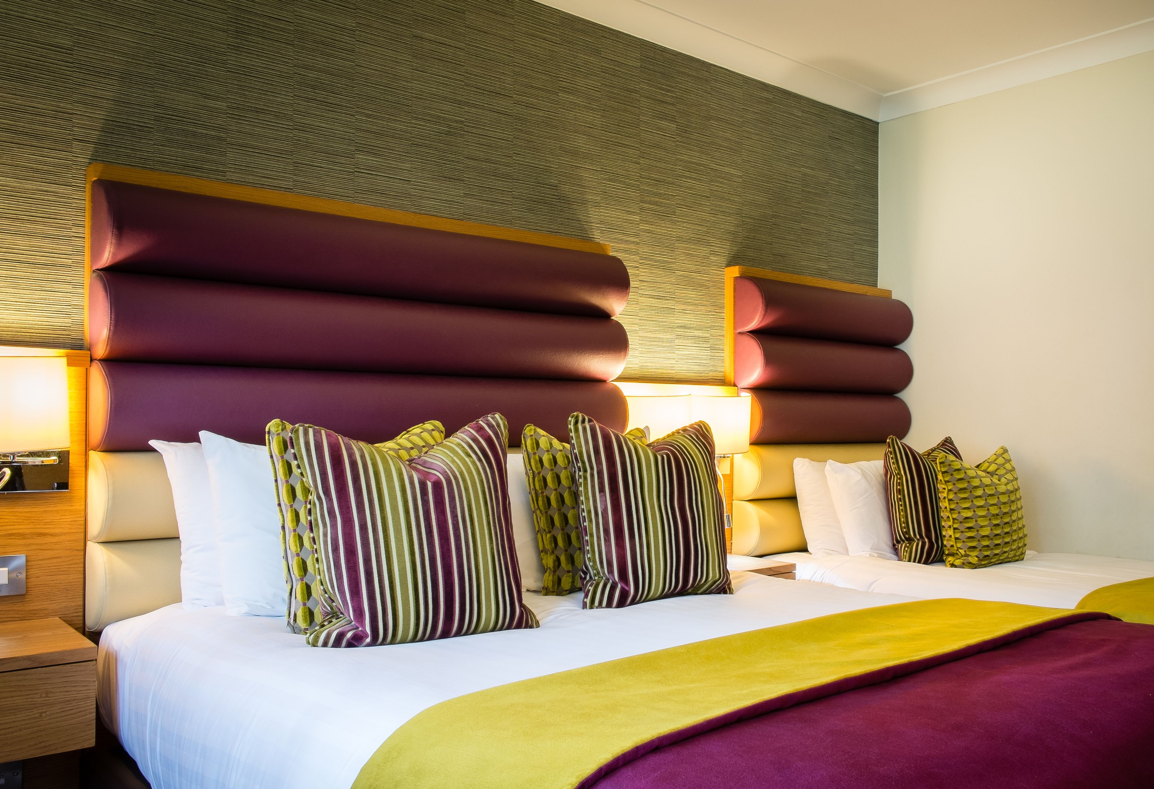 Une chambre d’hôtel avec un grand lit, plusieurs oreillers, une table de chevet en bois et une tête de lit fixée au mur.