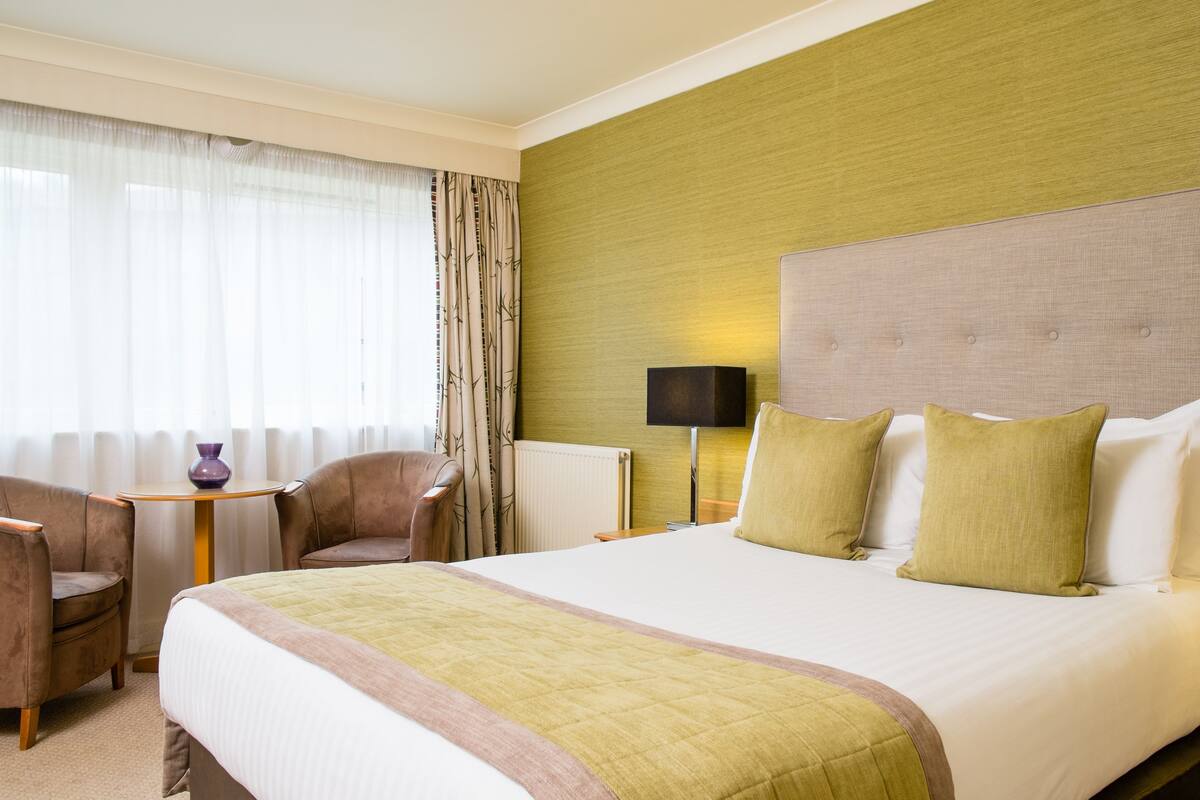 Une chambre d’hôtel avec un grand lit, deux fauteuils, une petite table et une lampe.
