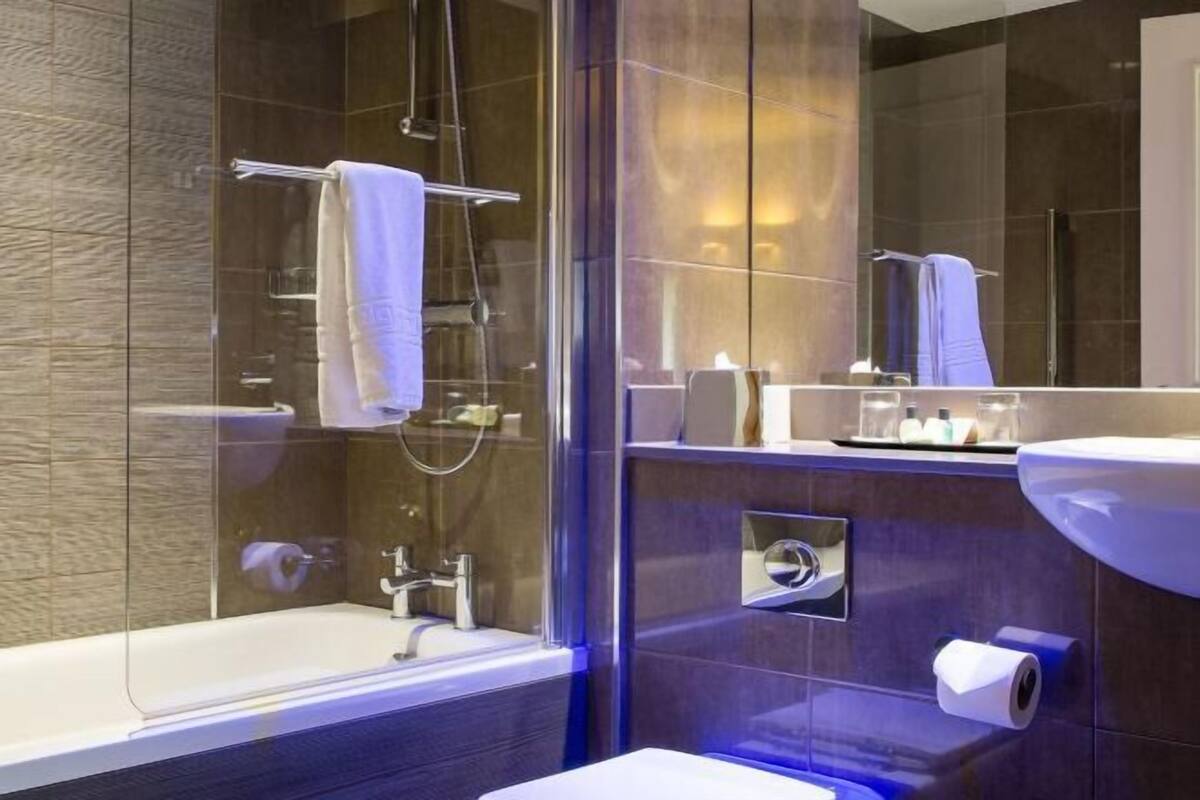 Une salle de bain moderne dotée d’une douche à parois de verre, d’une baignoire blanche, d’un grand miroir et d’un lavabo avec un porte-serviettes.