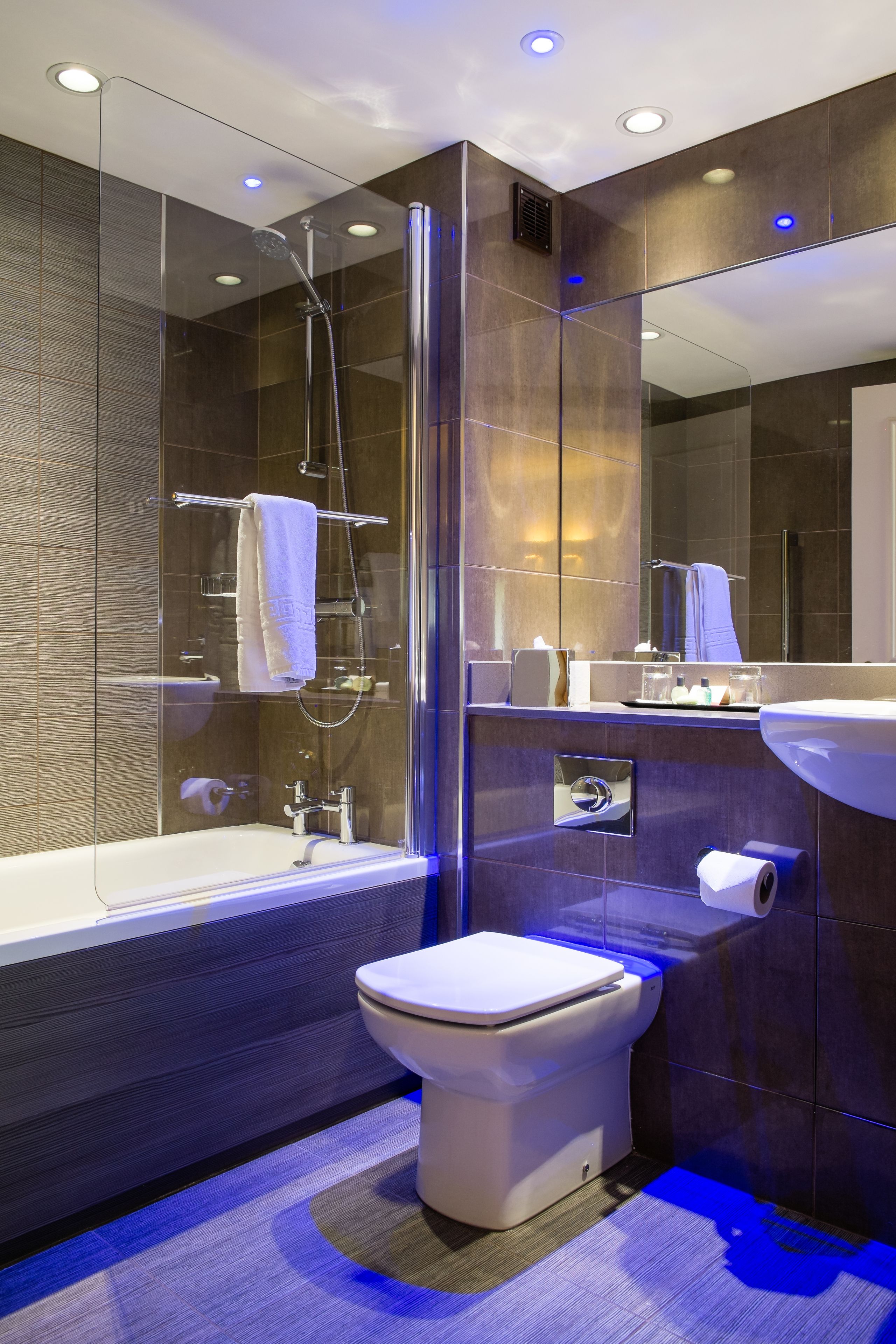 A modern bathroom with a glass-enclosed shower, a white toilet, and a large mirror.