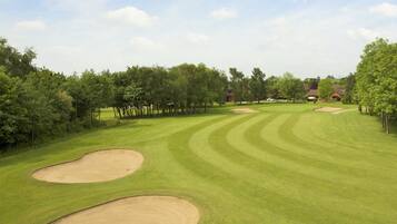 A golf course with bunkers, trees, and a building in the background.