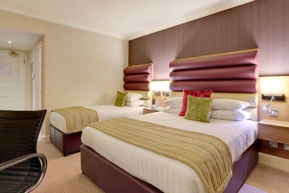Une chambre d’hôtel avec deux lits, une chaise et une table de chevet avec des lampes.