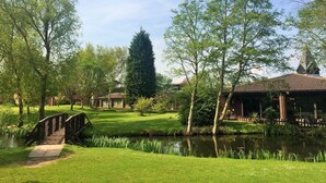 A serene park with a pond, a wooden bridge, and a building with a tiled roof. - Lea Marston Hotel (Sutton Coldfield)