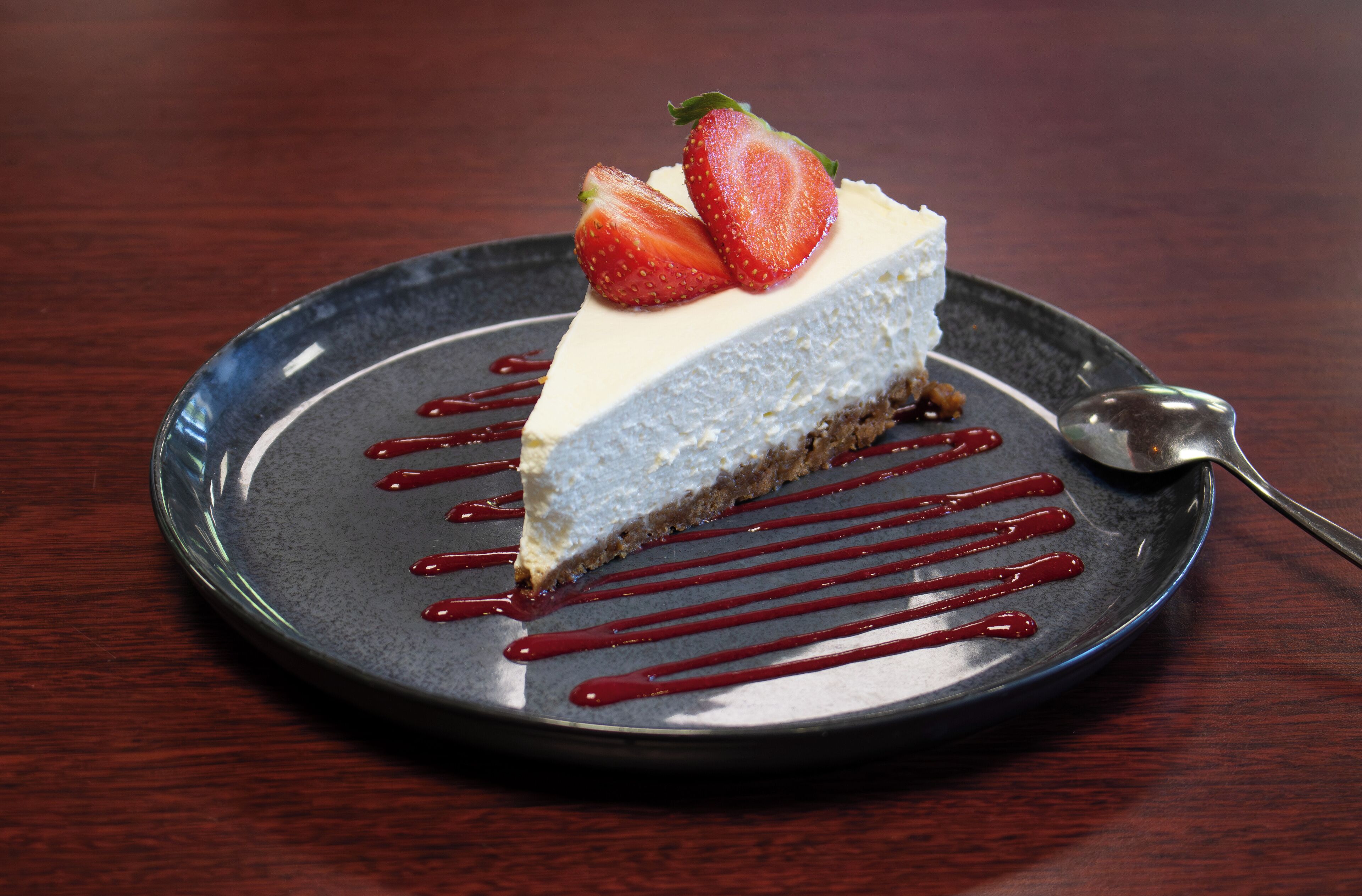 Una porción de pastel de queso con fresas y salsa de frutos rojos sobre un plato.