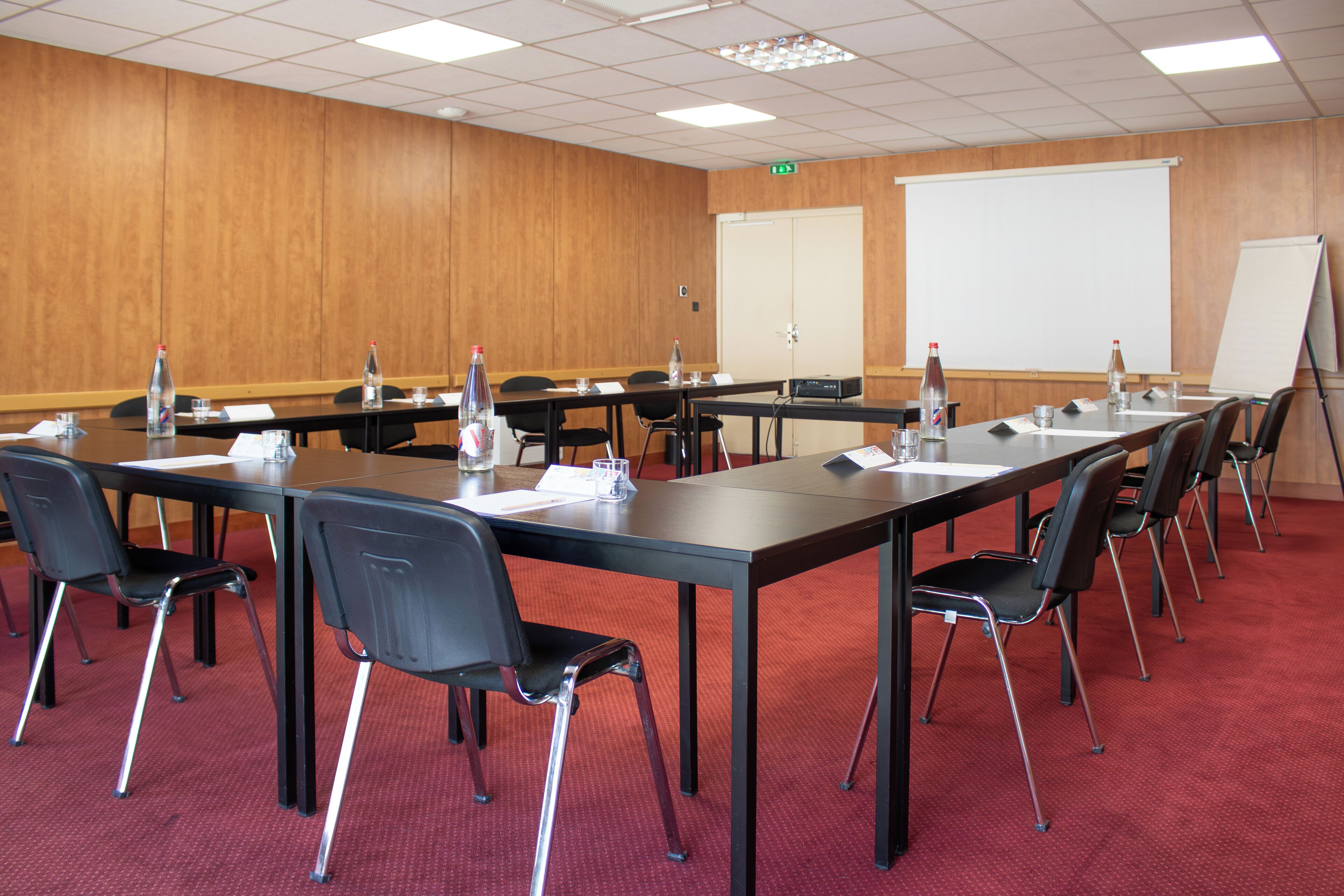 Une salle de conférence avec de longues tables, des chaises noires et un tableau blanc.