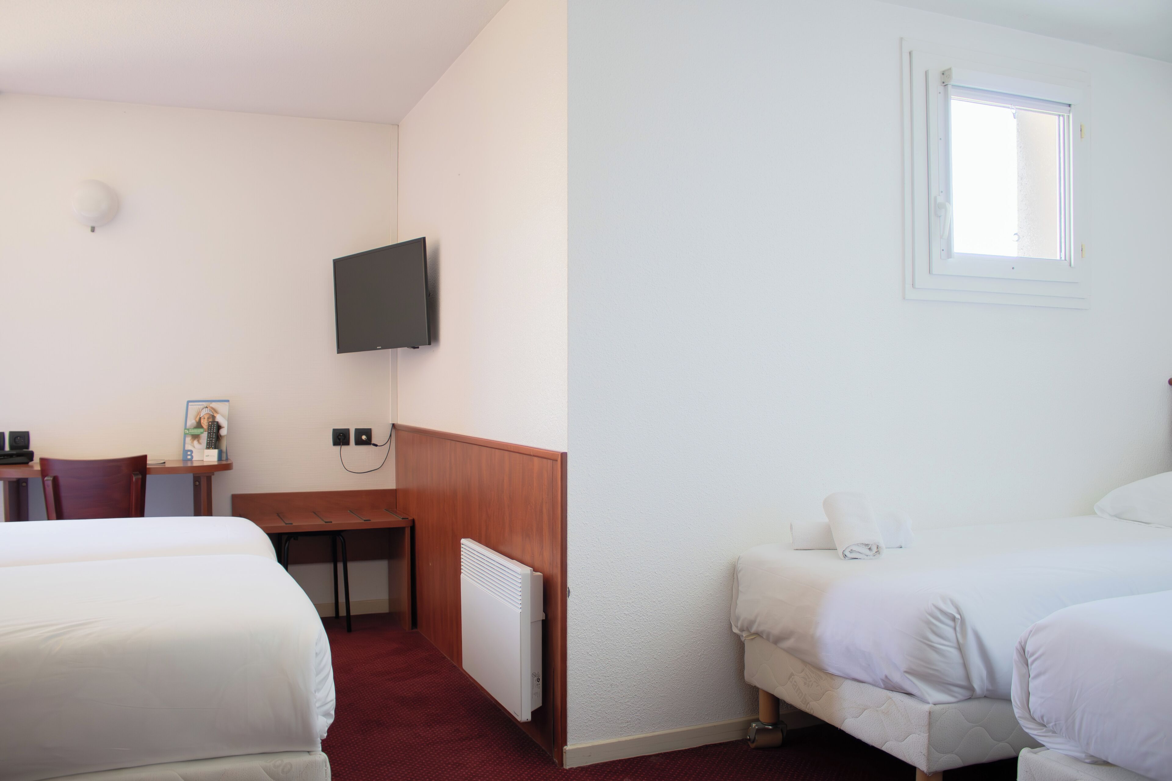 Habitación de hotel con dos camas, un escritorio, una silla, un televisor y una ventana.