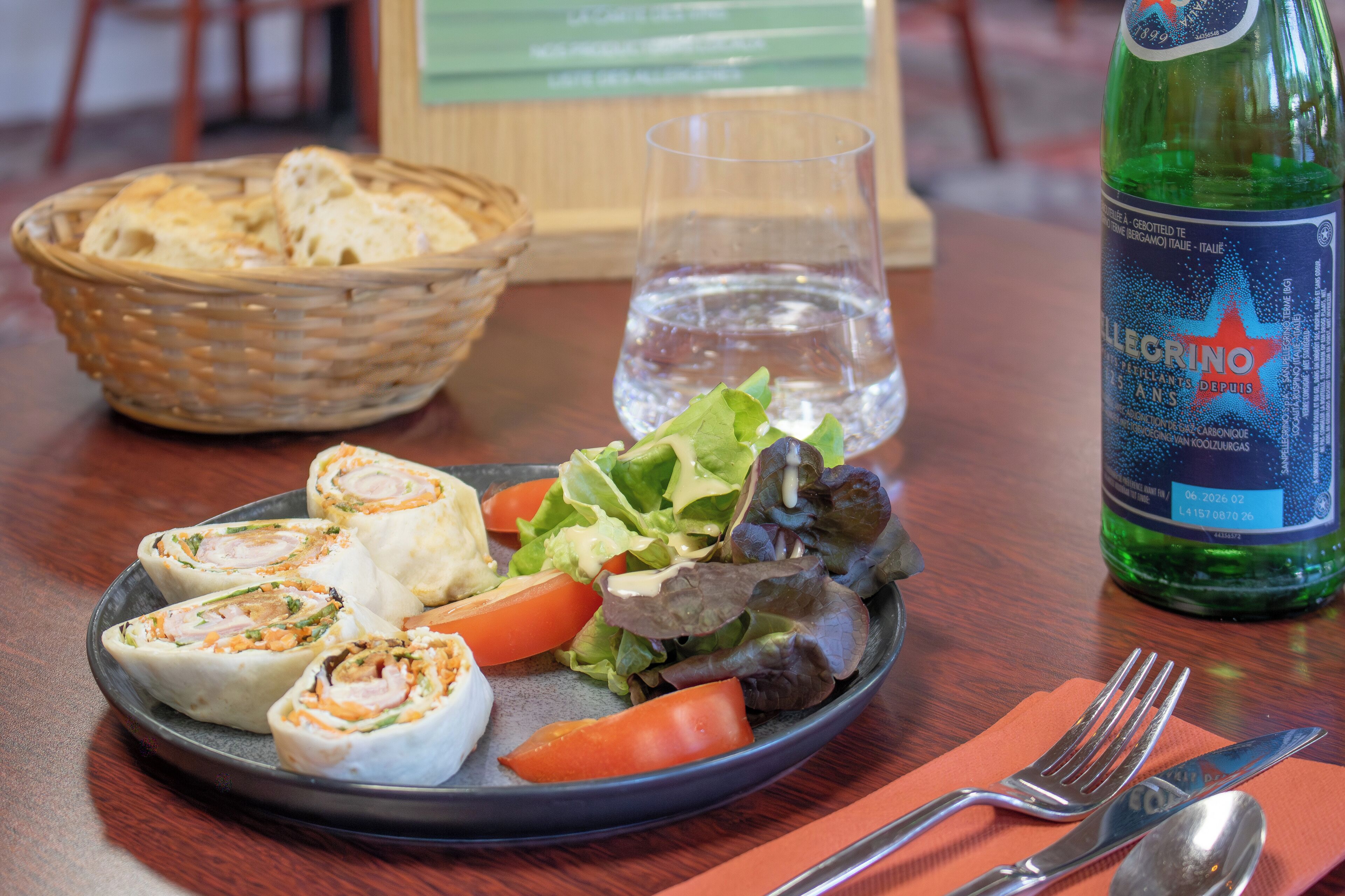 En tallerken mad med brød, salat og tomater, et glas vand og en vandflaske på et bord.
