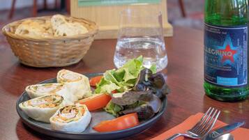 En tallerken mad med brød, salat og tomater, et glas vand og en vandflaske på et bord.