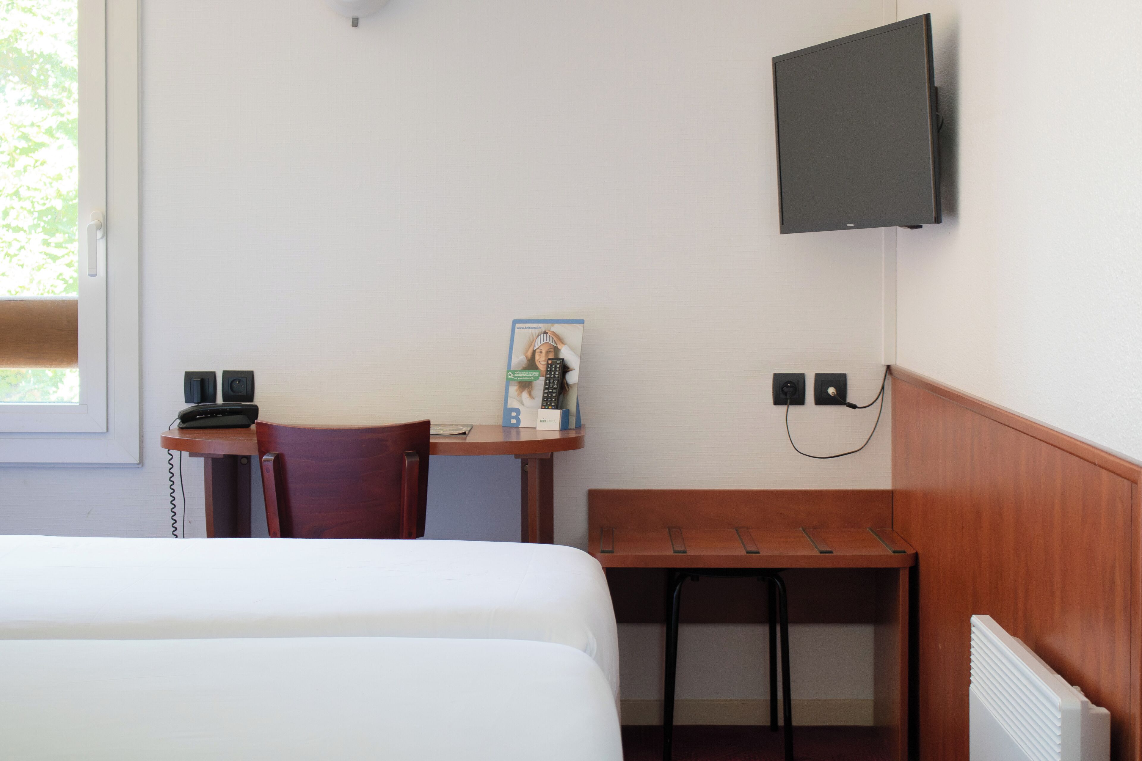 Habitación de hotel con cama, escritorio con teléfono, silla, mesita y televisor montado en la pared.