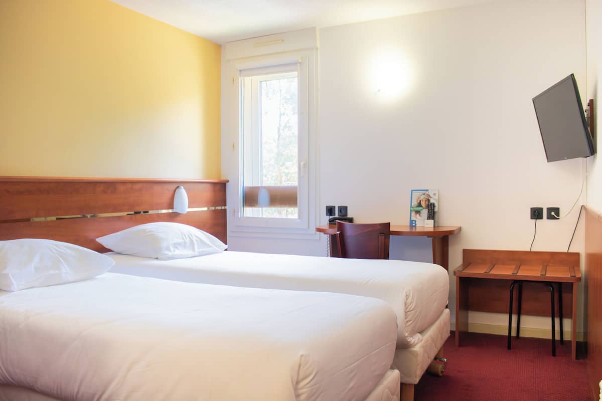 Een hotelkamer met twee bedden, een bureau, een stoel, een aan de muur bevestigde televisie en een raam.