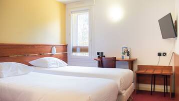 A hotel room with two beds, a desk, a chair, a TV mounted on the wall, and a window.