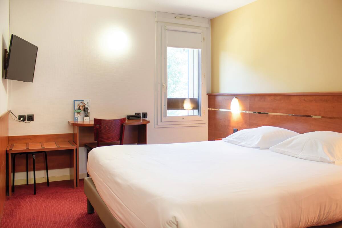 Een hotelkamer met een bed, bureau, stoel, televisie en raam.