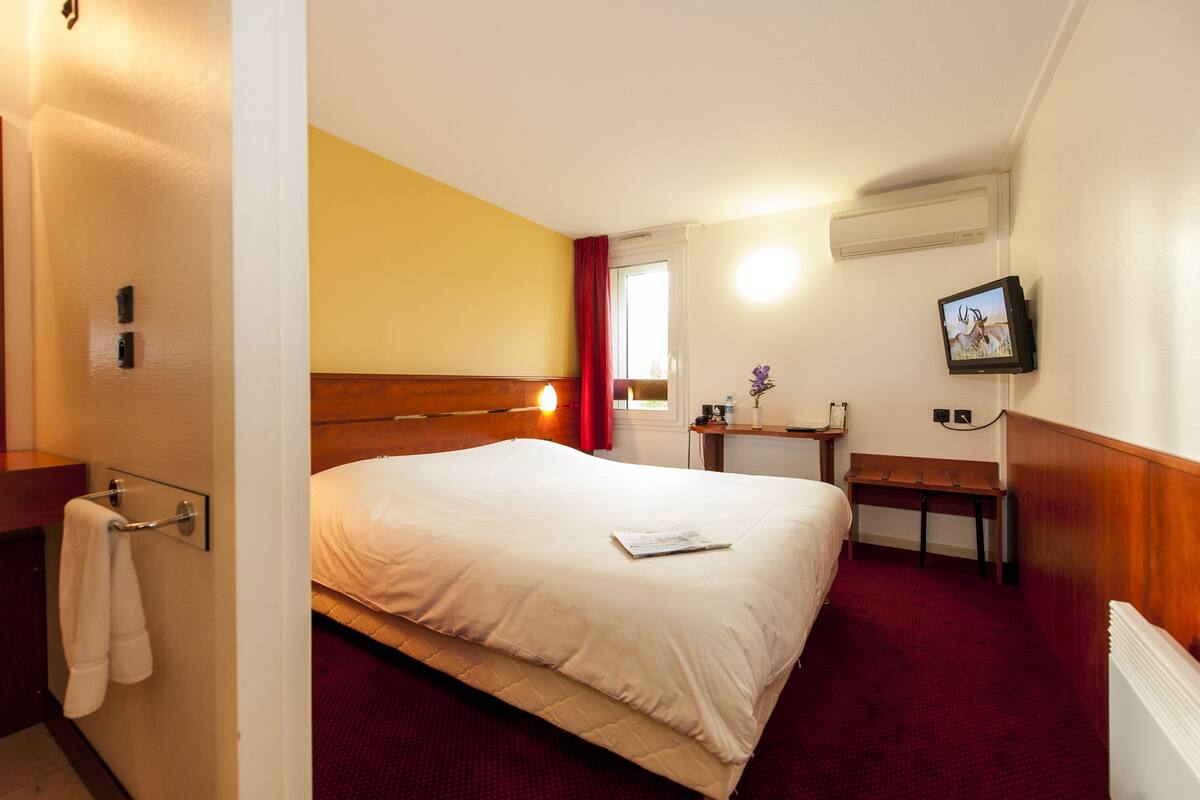 Een hotelkamer met een bed, nachtkastje, televisie en een raam met gordijnen.