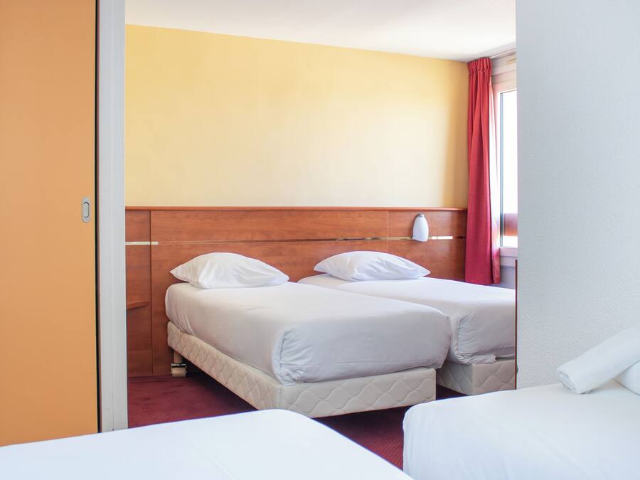 Habitación de hotel con dos camas, cabecera de madera y cortina roja.