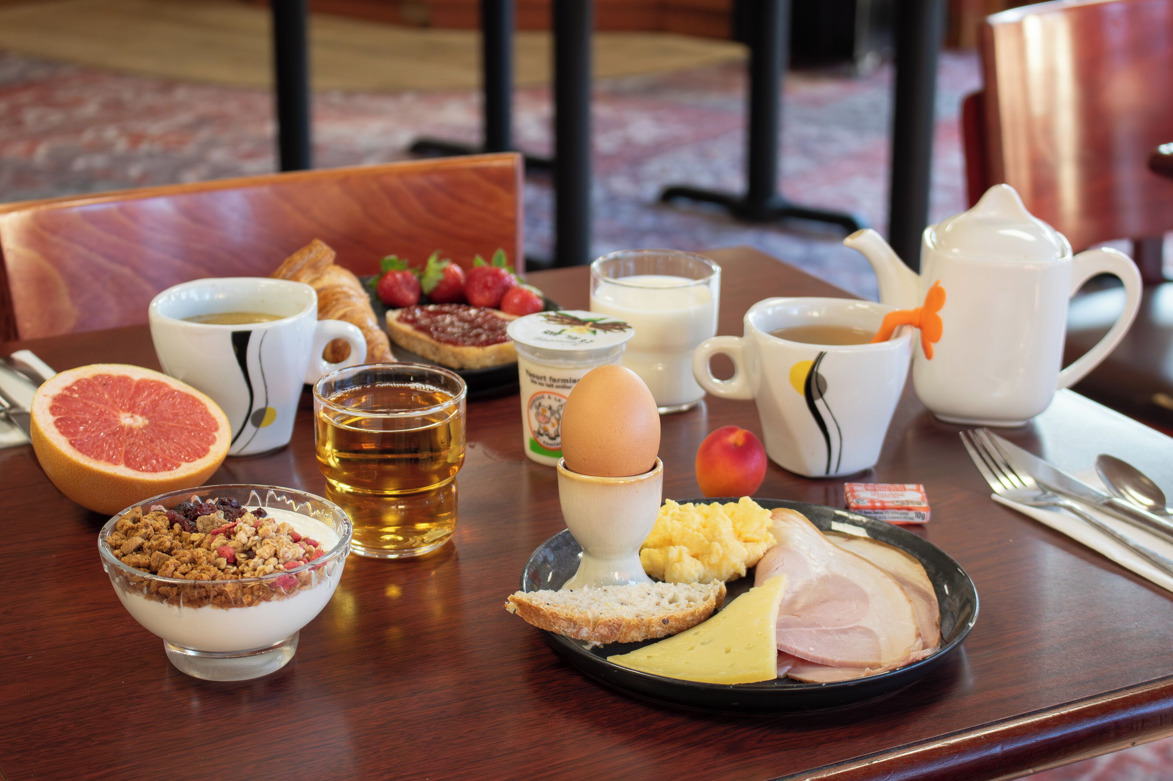 A breakfast tray with various foods and drinks, including a grapefruit, toast, cheese, ham, and a bowl of cereal.