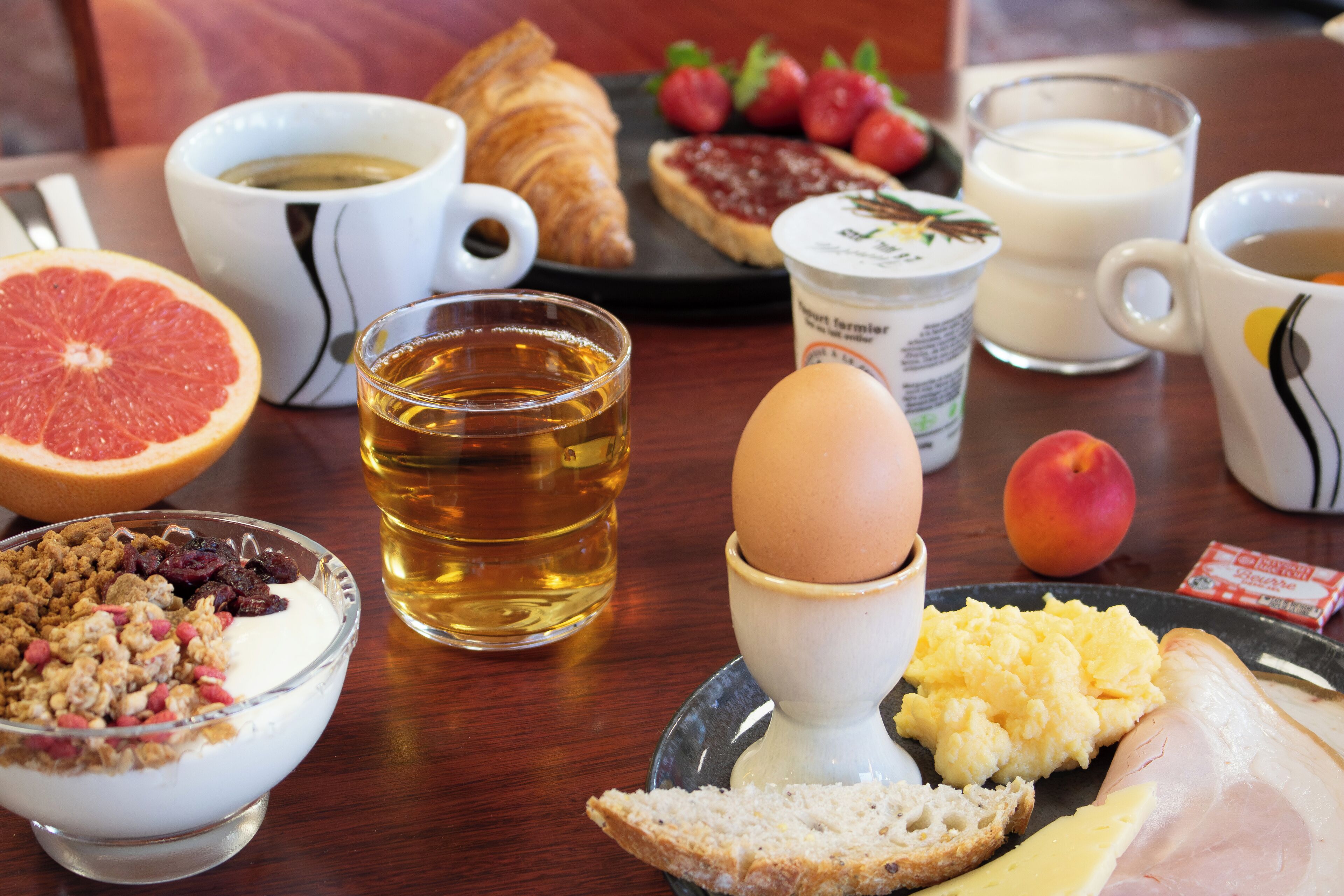 Ein Frühstückstisch mit verschiedenen Speisen, darunter ein Croissant, eine Grapefruit, Rührei, Toast und ein Glas Milch.