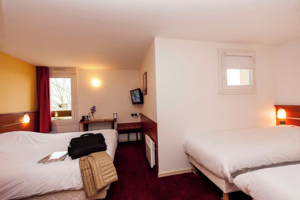 A hotel room with two beds, a desk with a chair, a TV, and a window.