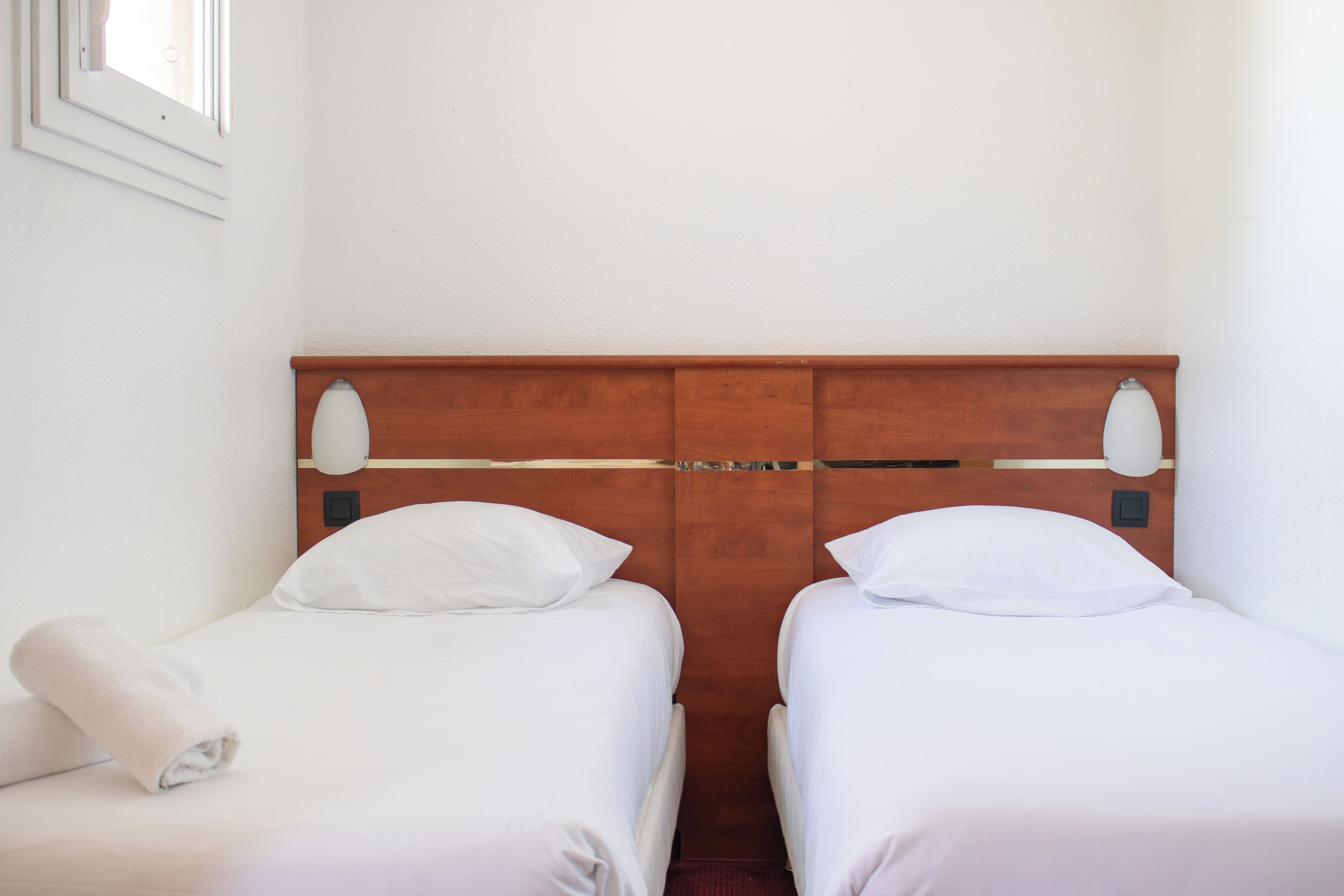 Two single beds with wooden headboards, white bedding, and a white towel on the left bed.