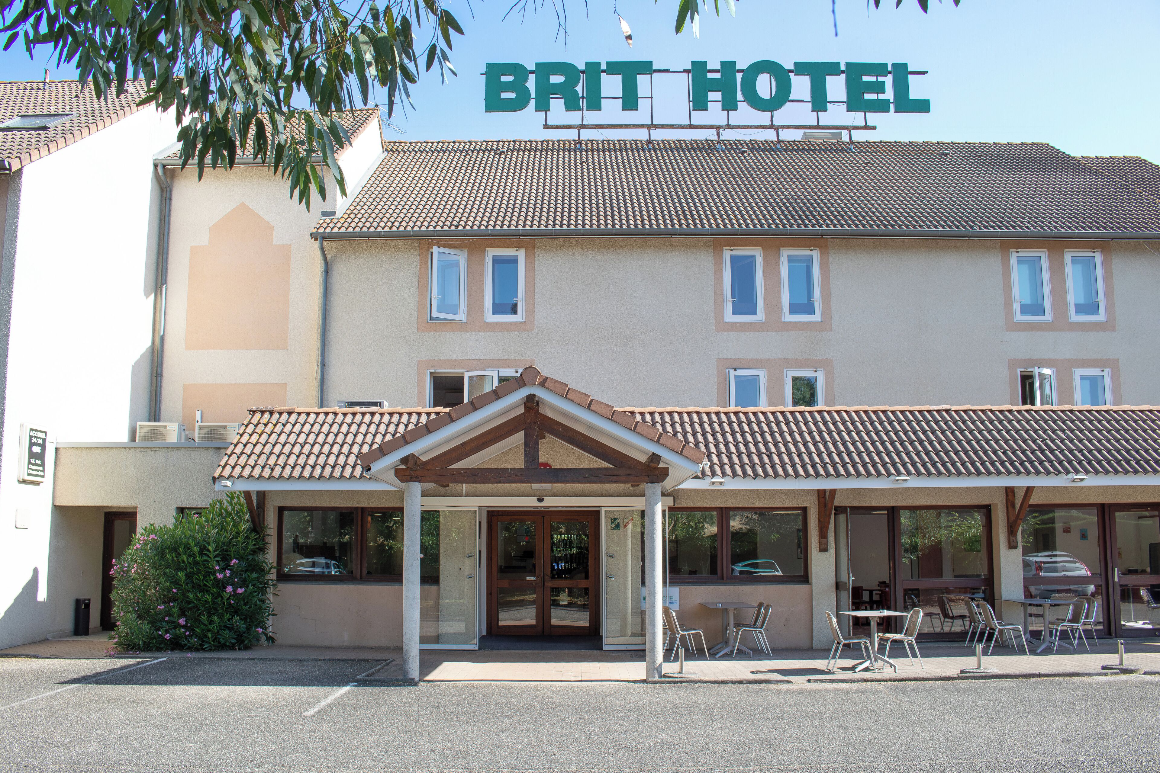 Un hôtel avec une enseigne « BRIT HOTEL » au-dessus de l’entrée, un espace extérieur abrité avec des sièges et un parking.