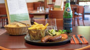 Una mesa de comedor con un cesto de pan, un plato de salchichas y papas fritas, una botella de agua Pellegrino y un menú.