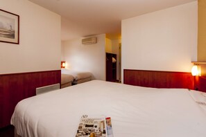A hotel room with a large bed, a bedside table, a wall-mounted air conditioner, and a framed picture on the wall.