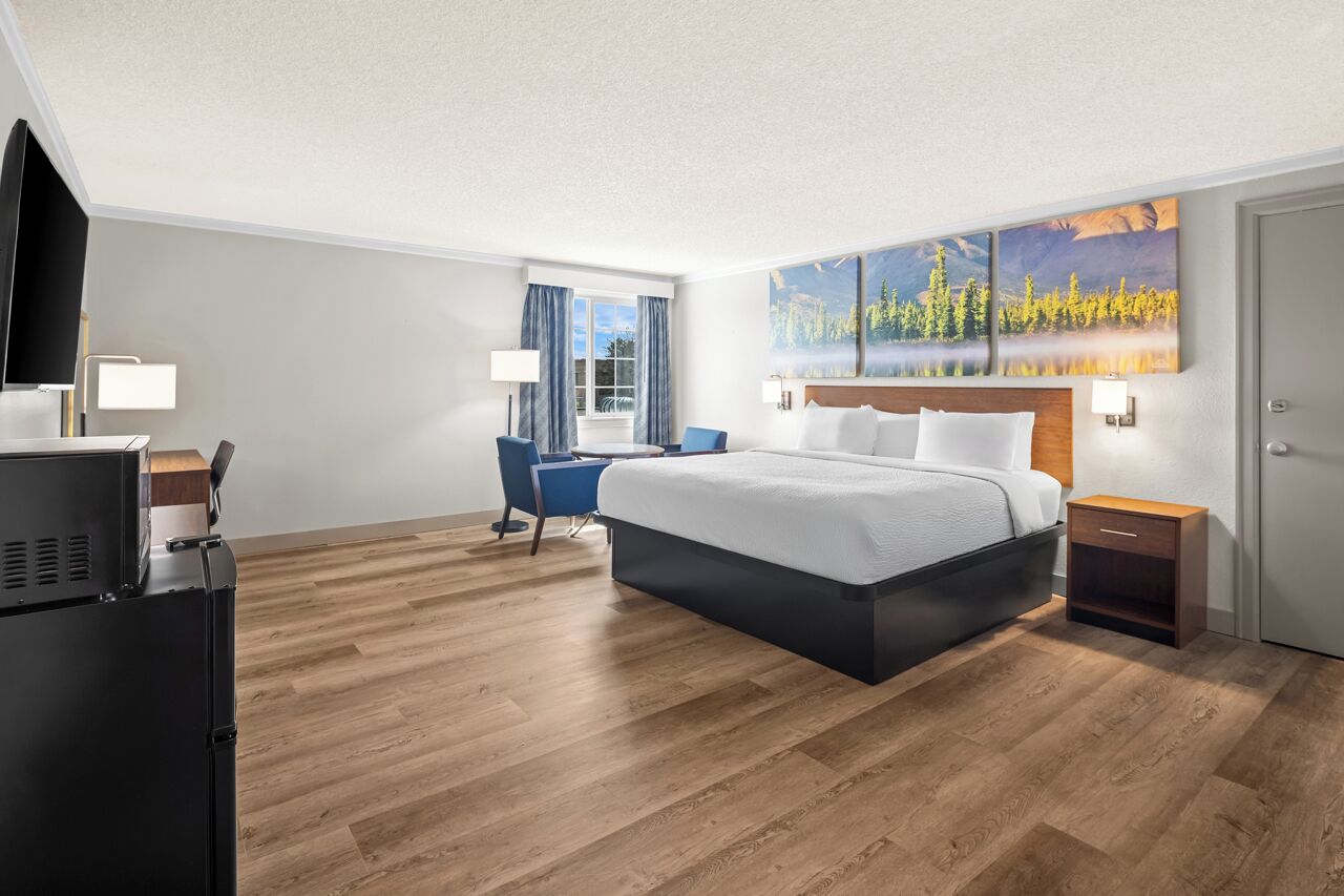A hotel room with a bed, a desk, a chair, a TV, and a painting on the wall.
