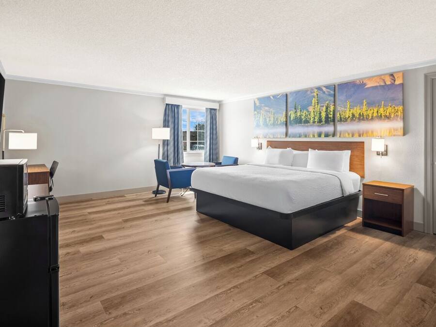 A hotel room with a bed, a desk, a chair, a TV, and a painting on the wall.