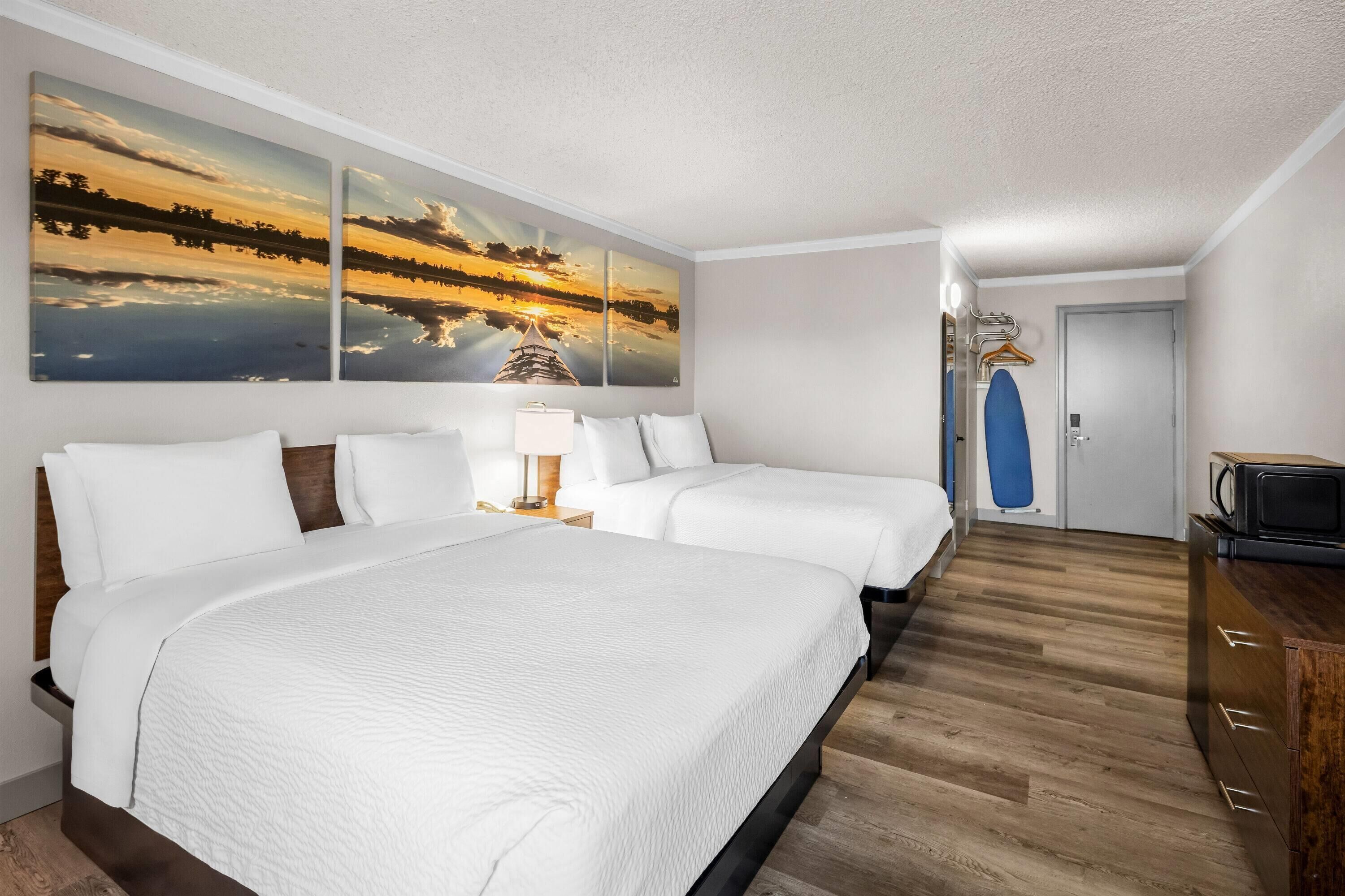 Habitació d'hotel amb un llit gran, dos llits més petits, terra de fusta, un televisor i una porta amb una tovallola blava penjant.