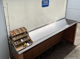 Un banco con espacio de almacenamiento y compartimentos que contienen equipo de pesca, y un cartel que indica que se pueden obtener bolsas para peces en la recepción.