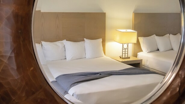Un miroir rond reflétant une chambre d’hôtel avec un lit, une table de chevet et une lampe.