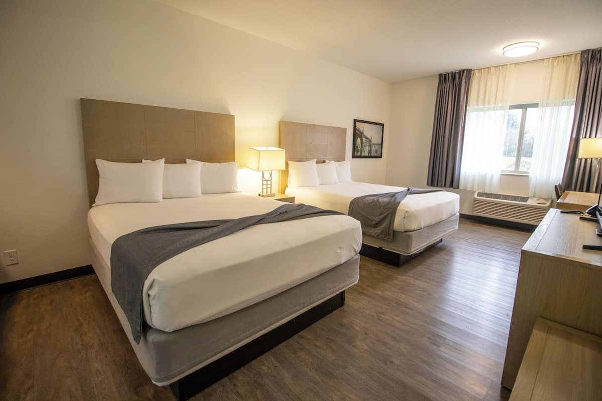 A hotel room with two beds, a desk, a chair, a lamp, and a window with curtains.