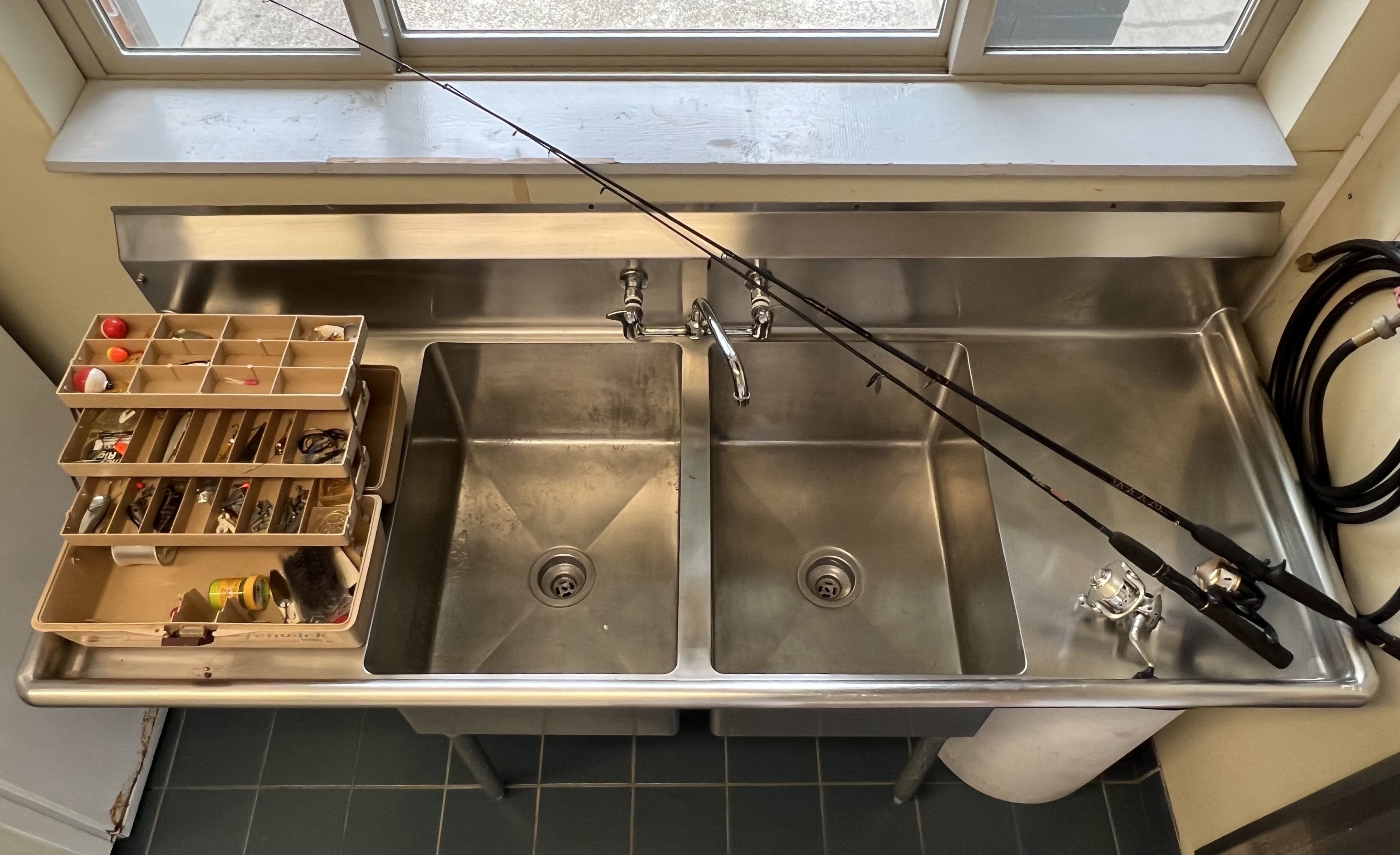 A kitchen with two stainless steel sinks, a window above, and a storage unit with various kitchen utensils.