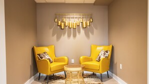 Une pièce avec deux chaises jaunes, une table ronde en bois, un tapis moelleux et un luminaire fixé au mur.