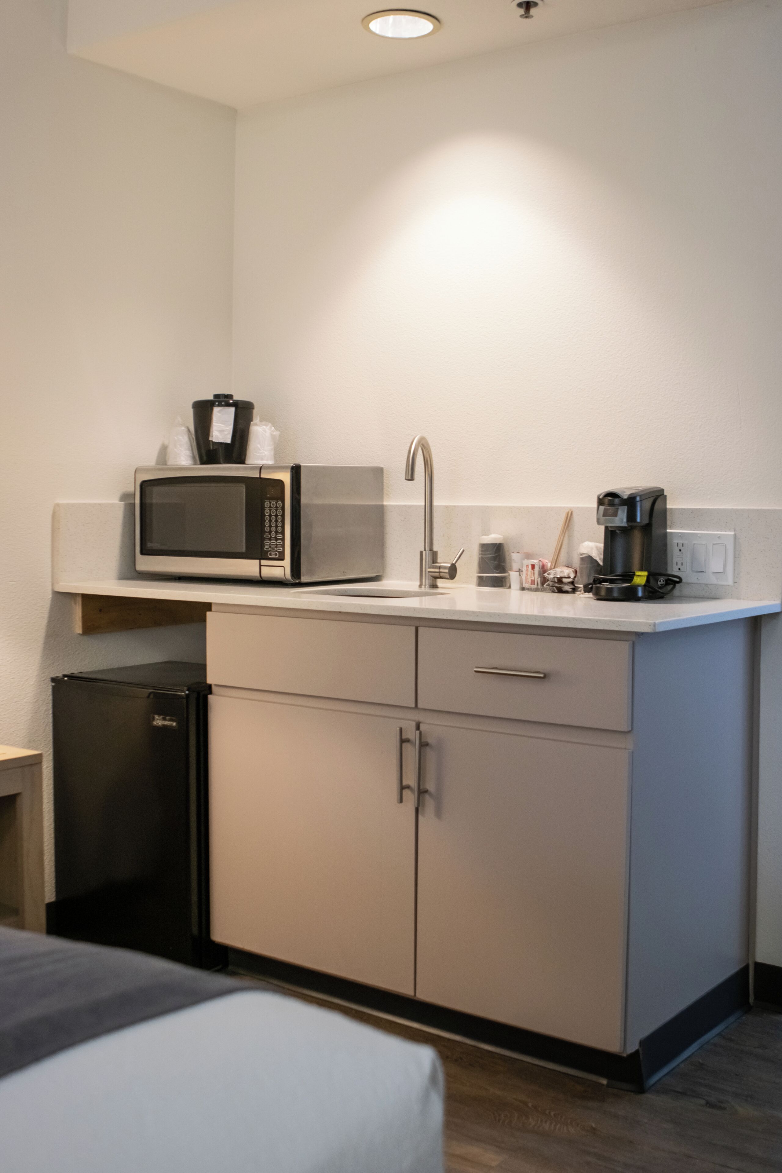 Een compact keukenhoekje met een magnetron, koffiezetapparaat en een kleine koelkast.