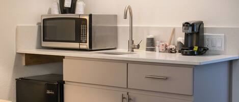 Una kitchenette compacta con microondas, cafetera y un refrigerador pequeño.