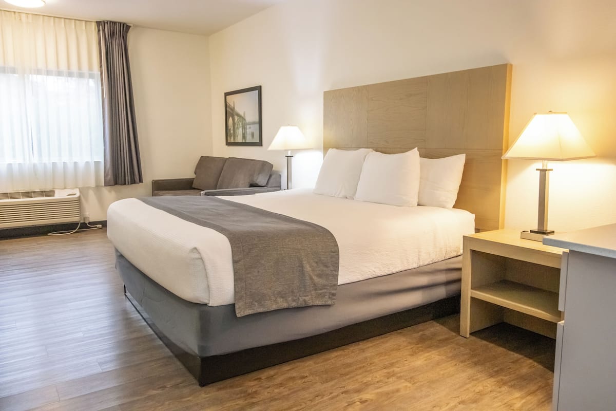 A hotel room with a bed, bedside tables, a sofa, a lamp, a picture on the wall, and a window with curtains.