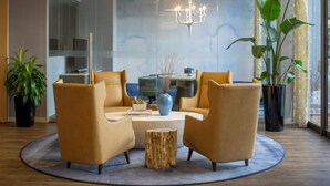 A modern living room with a round coffee table, two armchairs, a wooden stool, a blue vase, and a chandelier.
