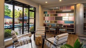A room with striped chairs, a wooden coffee table, a bookshelf, and a view of a pool area.