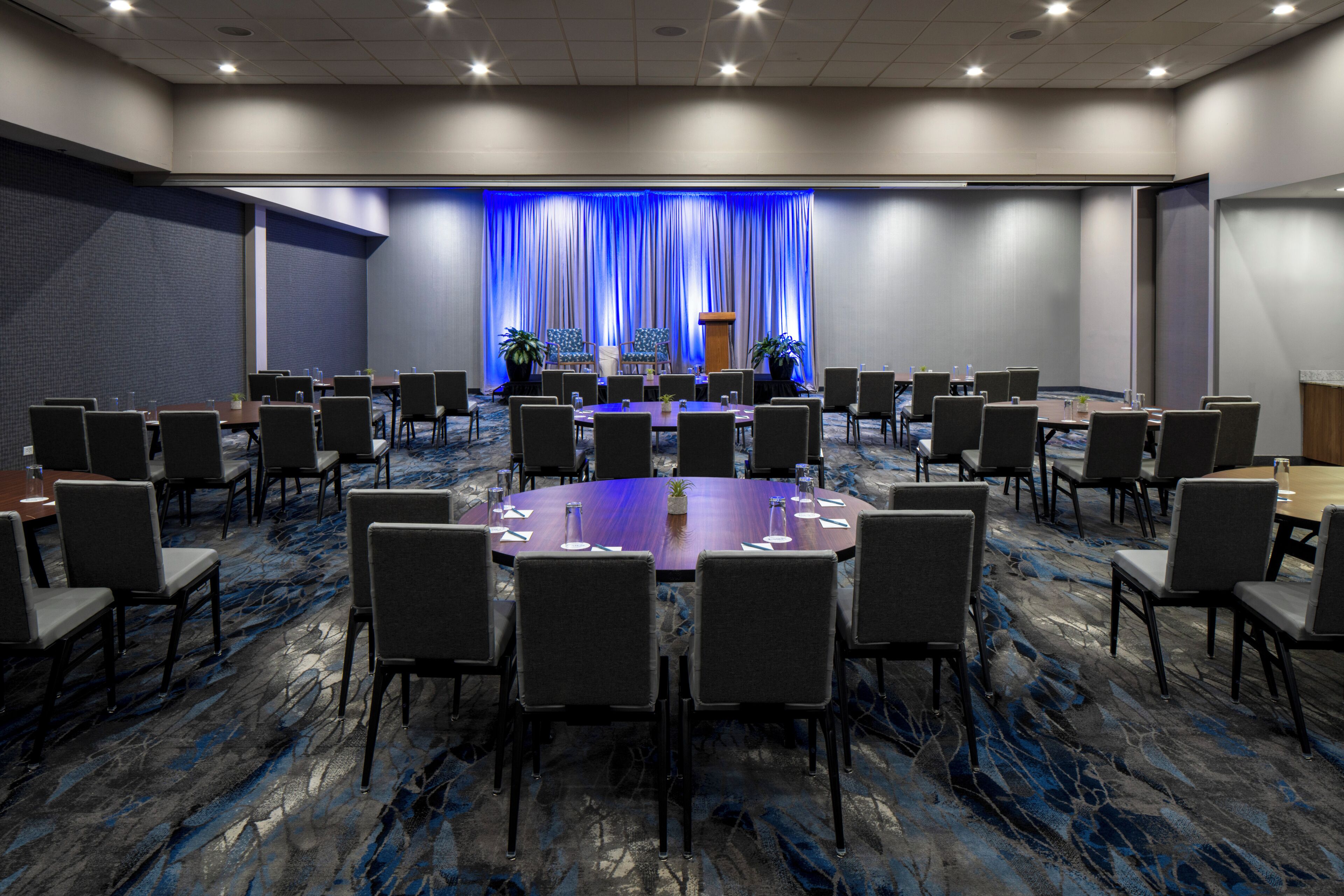 A conference room with a large oval table, multiple chairs, a podium, and a blue curtain backdrop.