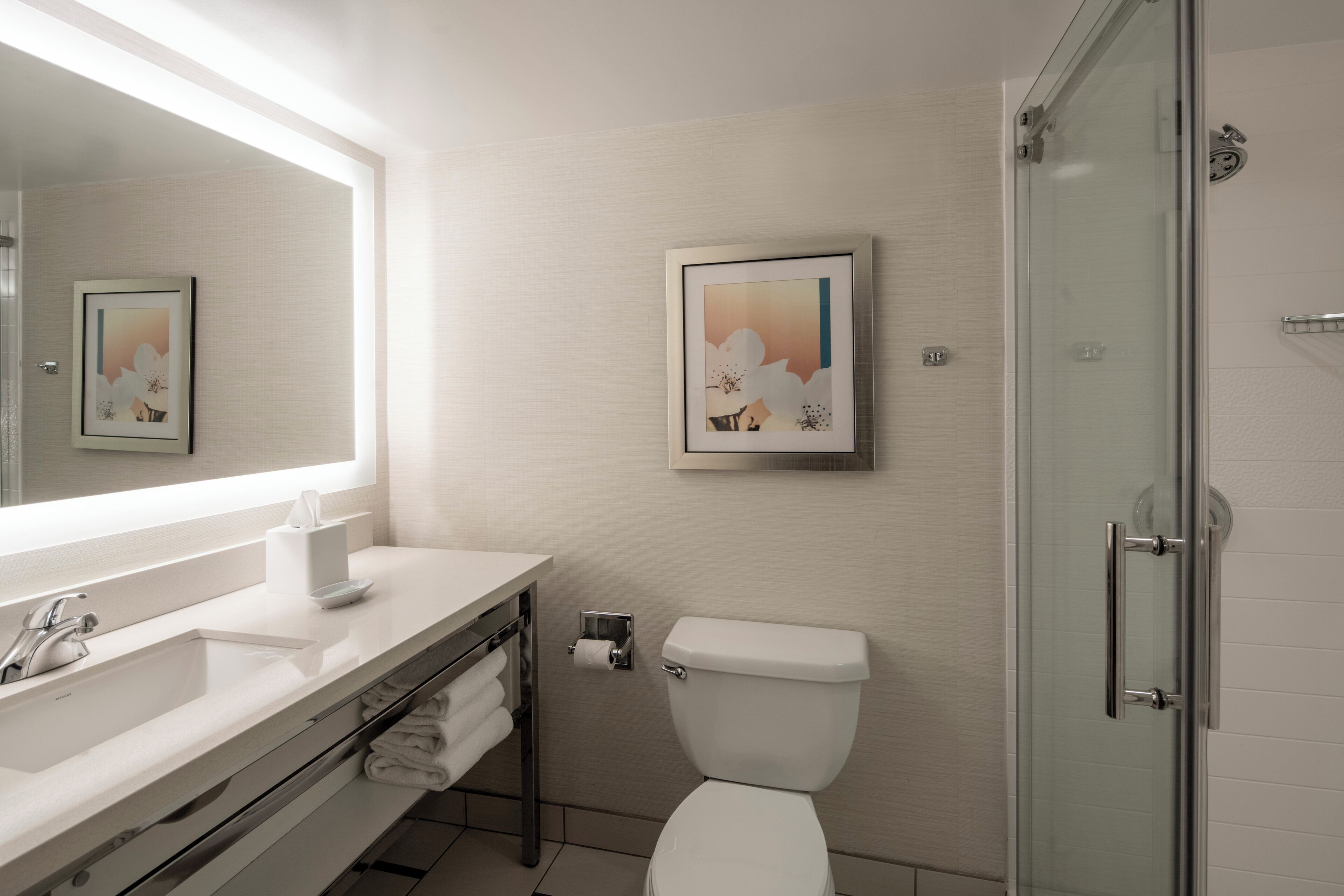 A bathroom with a white sink, mirror, toilet, and glass shower door.