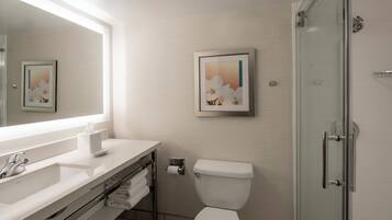A bathroom with a white sink, mirror, toilet, and glass shower door.
