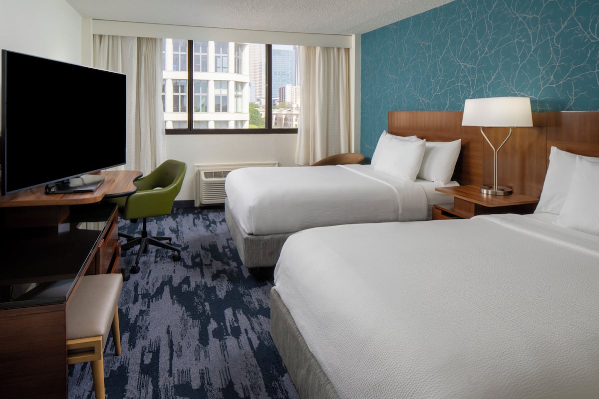 A hotel room with two beds, a TV, a desk, and a chair.