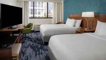 A hotel room with two beds, a TV, a desk, and a chair.