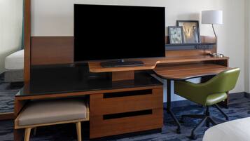 Ein Hotelzimmer mit Flachbildfernseher, Schreibtisch mit Stuhl, Nachttisch, Lampe und Bett.