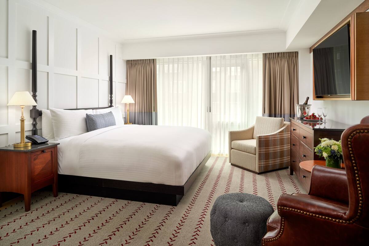 A hotel room with a large bed, a desk with a lamp, a chair, a dresser, and a television.